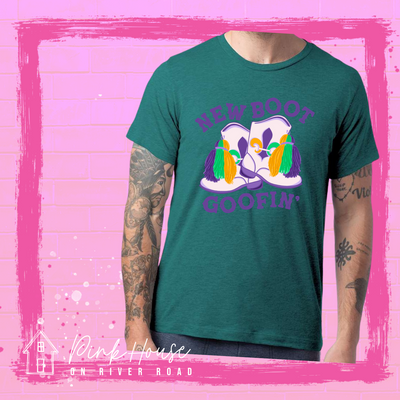 A green tee with a graphic. Graphic is of a pair of majorette boots, the boots have a tassel and fleur de lis both in gold, green and purple. the words New Boot are above the boots and the word goofin' is below thee boots the words are in purple.