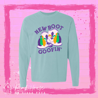 A seafoam green long sleeve tee with a graphic. Graphic is of a pair of majorette boots, the boots have a tassel and fleur de lis both in gold, green and purple. the words New Boot are above the boots and the word goofin' is below thee boots the words are in purple.