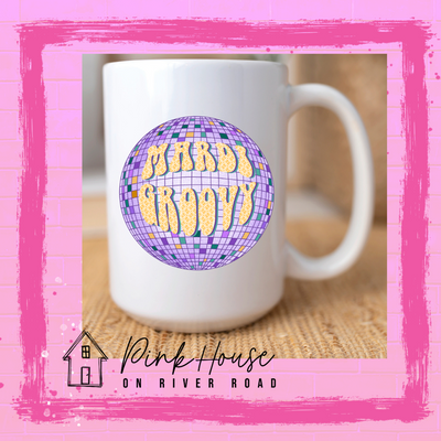 A white coffee mug with a light purple disco ball with various colors of purple, green, and yellow squares. The words Mardi Groovy in a 70s font with a yellow print on top of the disco ball.