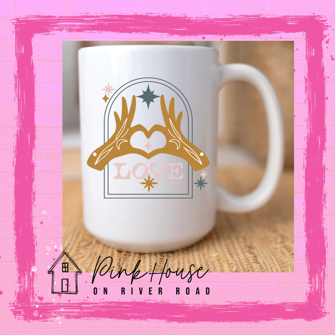 White Coffe mug with graphic. Graphic is of two tattooed hands making a heart in front of an archway with stars and the word Love in the archway