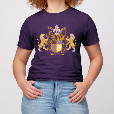 LSU Purple Tee. Alma Mater Classic family crest style hand drawn design. Crest has a tiger on each side with a banner below that reads Alma Mater with a fleur de Lis with filigree on top. Design is in LSU Purple and Gold