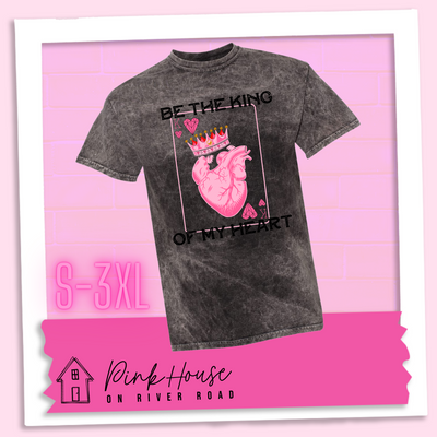 Black Mineral Wash Tee with a graphic that says "Be The King Of My Heart" in Black writing with a vintage effect. There is a King PLaying card with a speckled background, geometric hearts in the corners with the K and a realistic heart with a crown on it in the middle of the playing card.