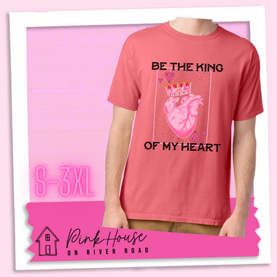 Coral Tee with a graphic that says "Be The King Of My Heart" in Black writing with a vintage effect. There is a King PLaying card with a speckled background, geometric hearts in the corners with the K and a realistic heart with a crown on it in the middle of the playing card.
