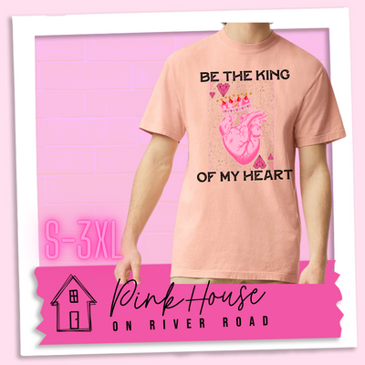 Peach Tee with a graphic that says "Be The King Of My Heart" in Black writing with a vintage effect. There is a King PLaying card with a speckled background, geometric hearts in the corners with the K and a realistic heart with a crown on it in the middle of the playing card.
