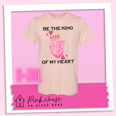 Heather Peach Tee with a graphic that says "Be The King Of My Heart" in Black writing with a vintage effect. There is a King PLaying card with a speckled background, geometric hearts in the corners with the K and a realistic heart with a crown on it in the middle of the playing card.