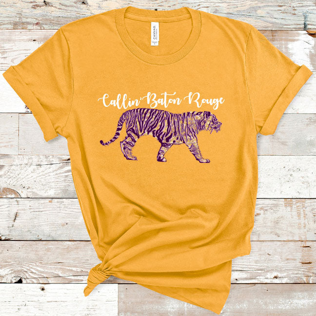 Gold Tee. Graphic has a tiger in the LSU colors of purple and gold text above the tiger reads callin baton rouge in cursive
