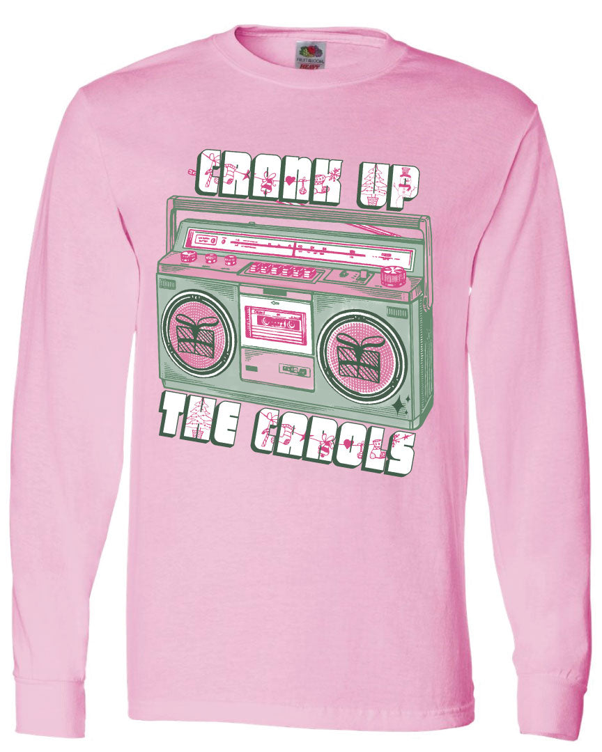 Pink long sleeve tee with graphic. Graphic has an old school boom box in the middle, the boom box is green with pink highlights and the speakers have the outline of presents on them. There is text above the boombox that is white with a green shadow and pink Christmas designs that says "Crank up" and below the boom box that says "The Carols"
