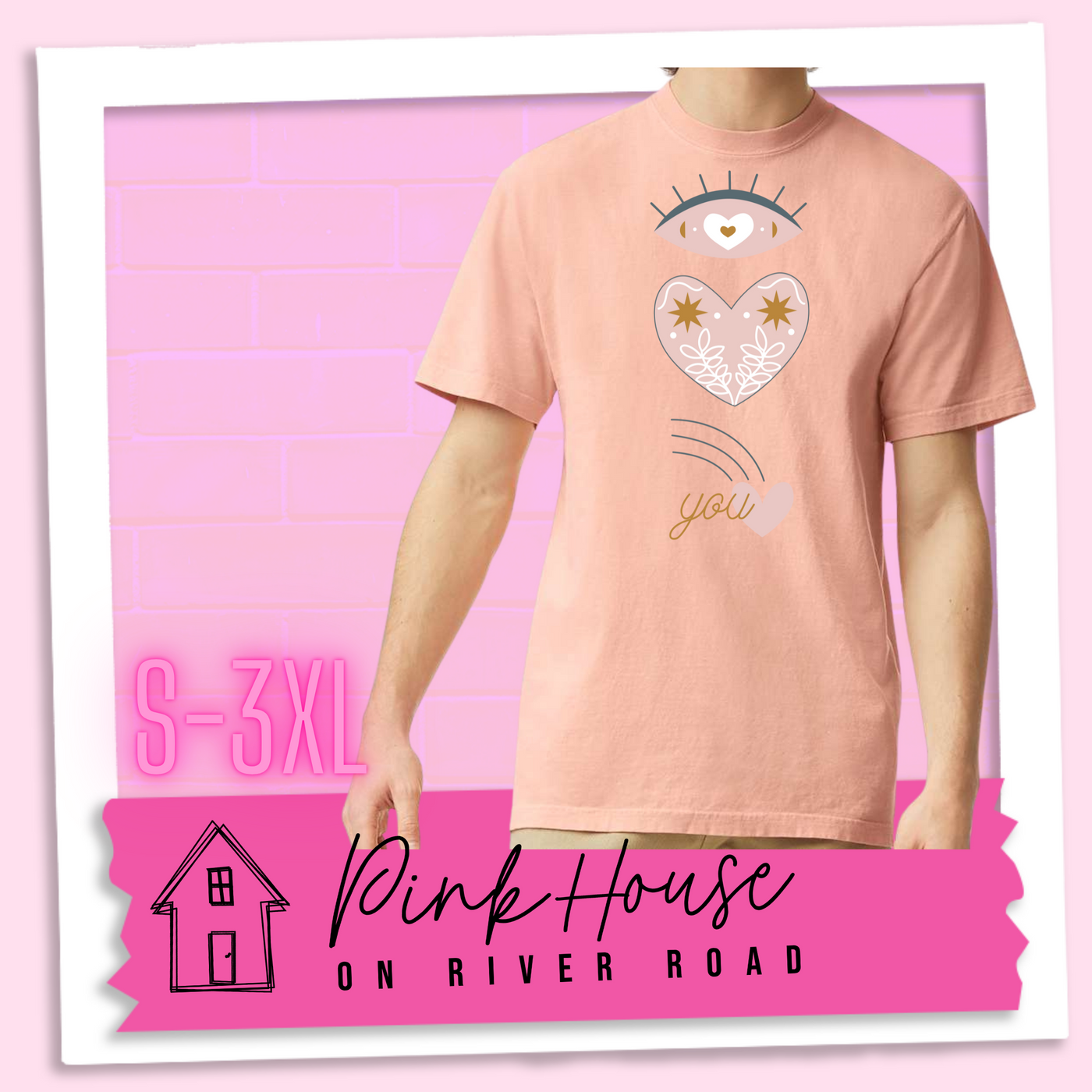 Peach tee with a graphic of an eye with a heart for the pupil and underneath that a heart with a floral and star design and a shooting heart with the word you. The graphic represents eye heart you