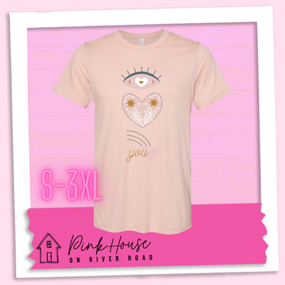 Heather Peach tee with a graphic of an eye with a heart for the pupil and underneath that a heart with a floral and star design and a shooting heart with the word you. The graphic represents eye heart you
