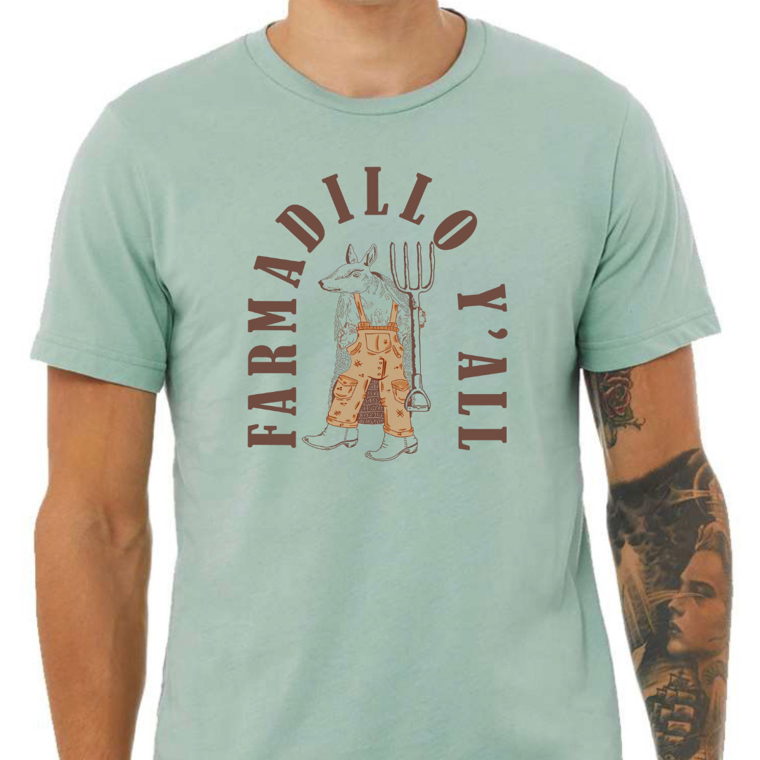 Dusty Blue tee with a graphic of an armadillo wearing tan overalls and a pair of boots holding a pitch fork. the words "Farmadillo Y'all" arching around the graphic.
