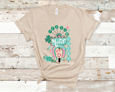 Heather Tan Tee. Graphic of a vintage Neon Sign The word feeling with each letter in green circles at the top with the word lucky down the side with each letter in a turquoise circle. There is a sign in the center with the word motel in it, underneath there is a horse shoe with dice inside at he bottom of the sign. There is also a four leaf clover with the word clover city over it in green.