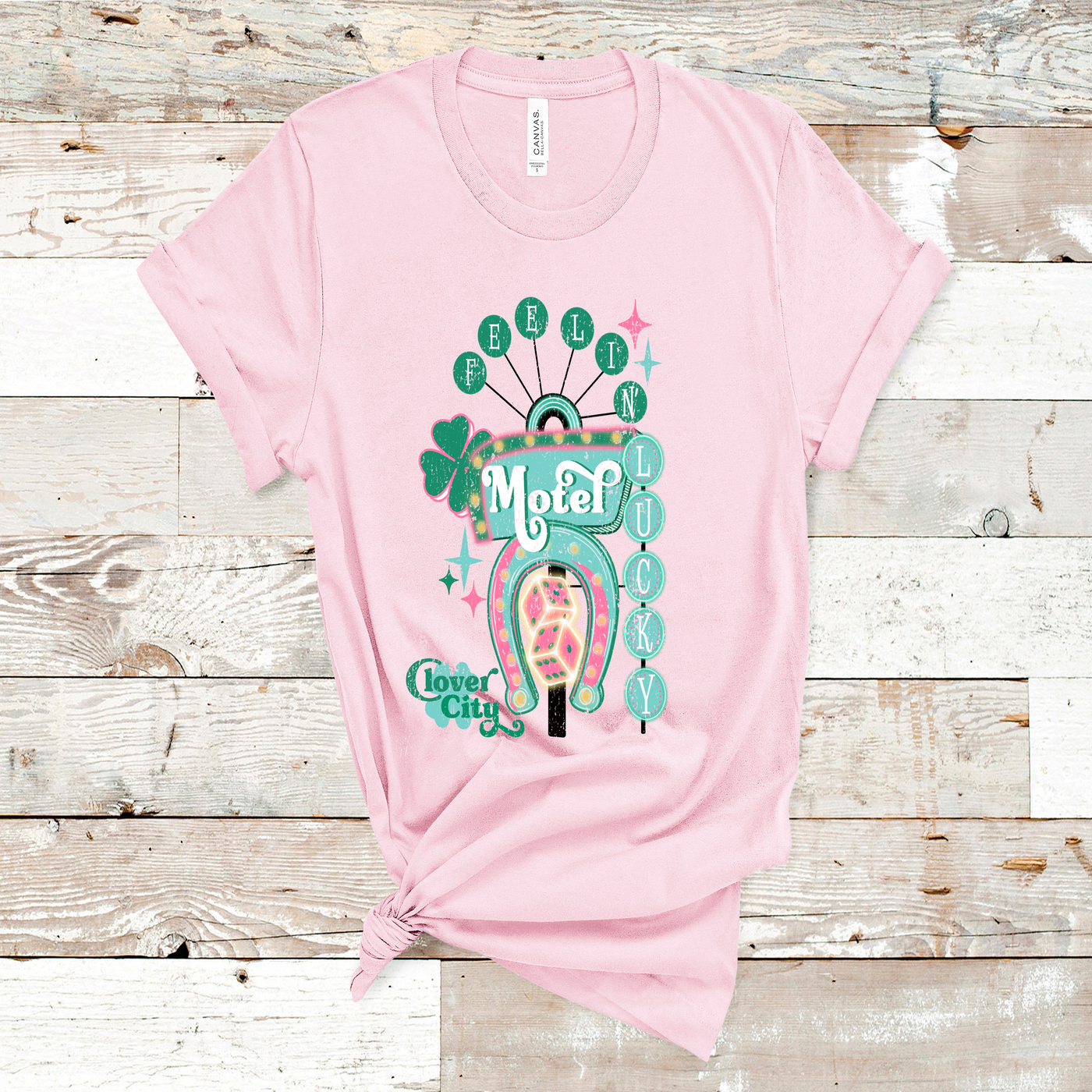 Pink Tee. Graphic of a vintage Neon Sign The word feeling with each letter in green circles at the top with the word lucky down the side with each letter in a turquoise circle. There is a sign in the center with the word motel in it, underneath there is a horse shoe with dice inside at he bottom of the sign. There is also a four leaf clover with the word clover city over it in green.