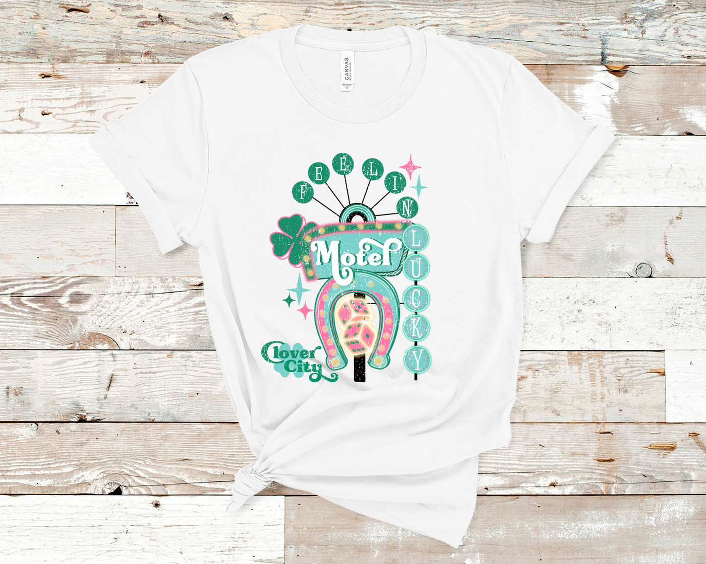 White Tee. Graphic of a vintage Neon Sign The word feeling with each letter in green circles at the top with the word lucky down the side with each letter in a turquoise circle. There is a sign in the center with the word motel in it, underneath there is a horse shoe with dice inside at he bottom of the sign. There is also a four leaf clover with the word clover city over it in green.