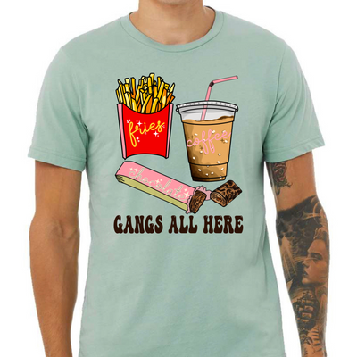Dusty Blue shirt with graphic. Graphic is a container of fries with a yellow cursive font that says fries. A cup of iced coffee with a pink cursive font that says coffee and a chocolate bar witha pink wrapper and a blue cursive font that says chocolate. Under the food there is a black bubble font that says gangs all here.