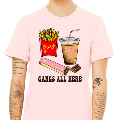 Soft Pink shirt with graphic. Graphic is a container of fries with a yellow cursive font that says fries. A cup of iced coffee with a pink cursive font that says coffee and a chocolate bar witha pink wrapper and a blue cursive font that says chocolate. Under the food there is a black bubble font that says gangs all here.