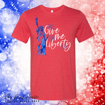 A heather red shirt with a graphic. Graphic is the statue of liberty to the right of it is firework explosions in blue as well as the words "Give me Liberty" In a white cursive font