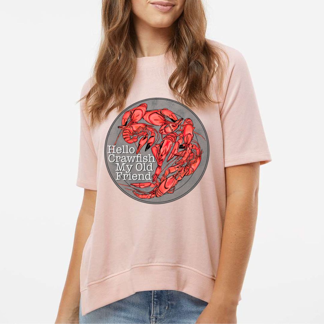 Light Peach French Terry Tee. Graphic is a grey plate full of crawfish and the words "Hello Crawfish My Old Friend" In a white font towards the bottom left of the plate