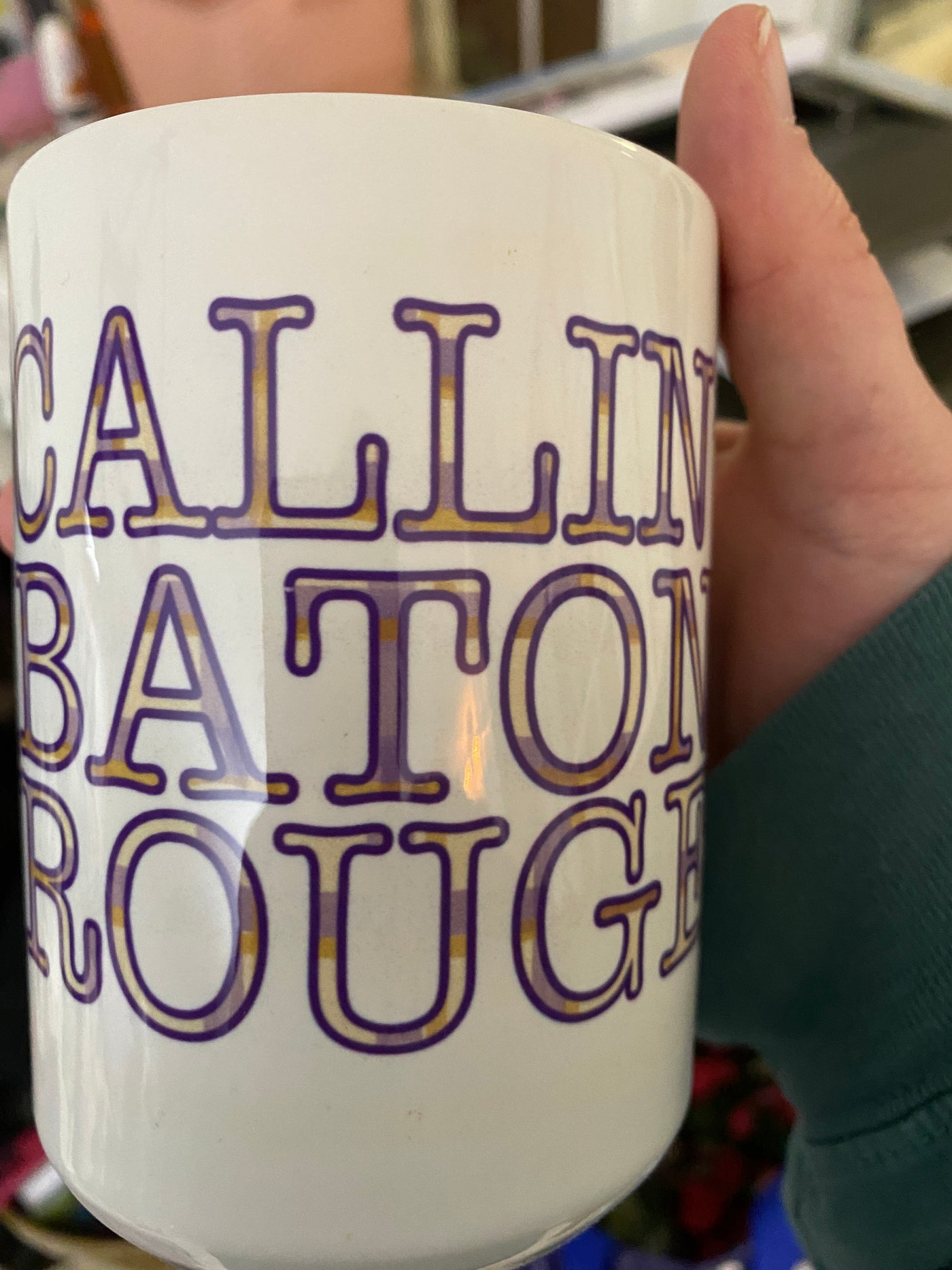 Hand holding a coffee mug. Coffee mug has plaid type that says "Callin Baton Rouge"