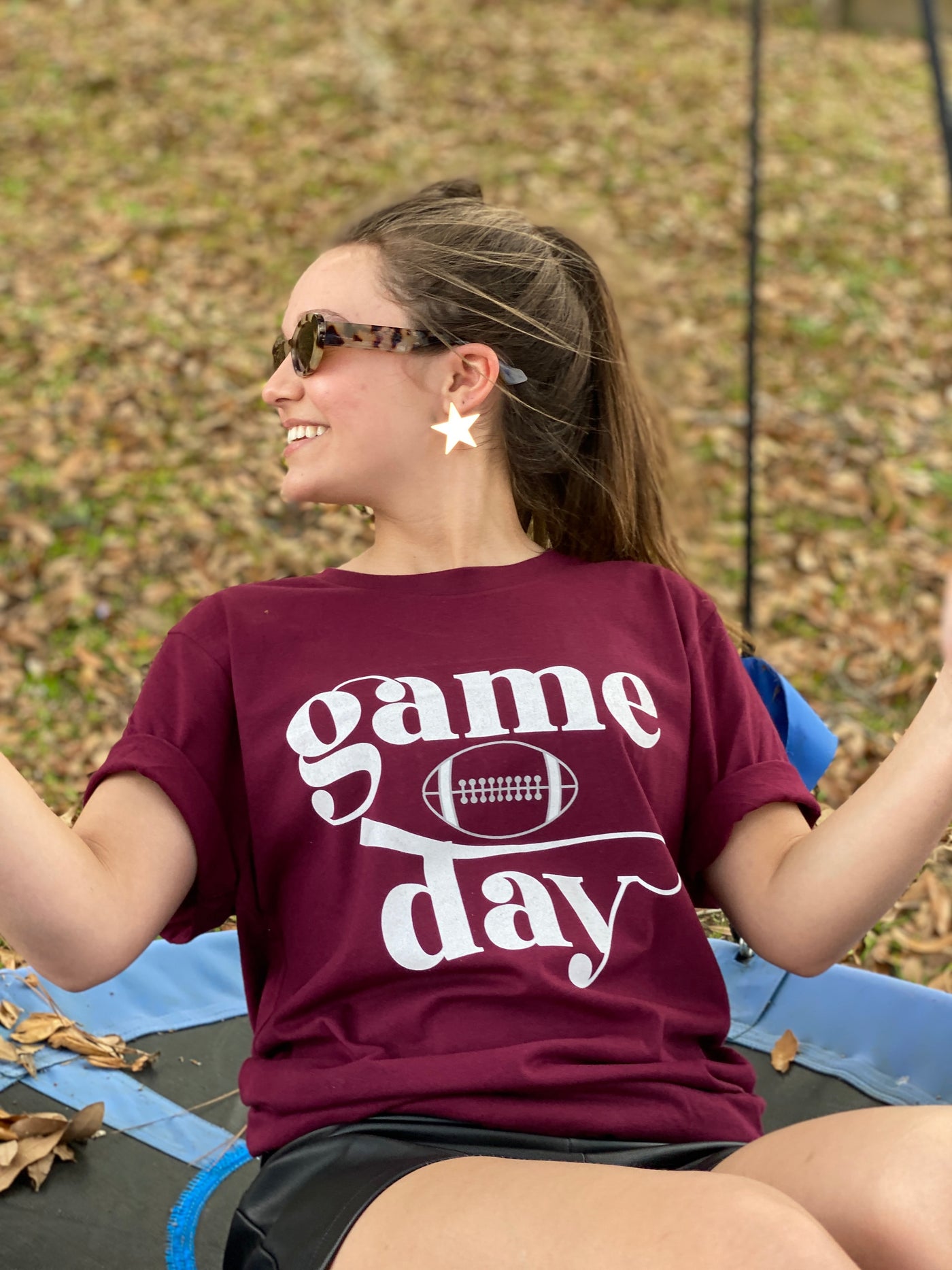 A maroon shirt with the word game stacked on top of a football stacked on top of the word day all in white.