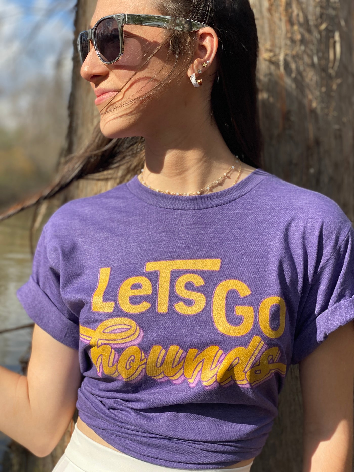 Heather purple shirt with the words lets go in yellow on top of the word hounds in a yellow retro cursive with a light yellow and purple shadow