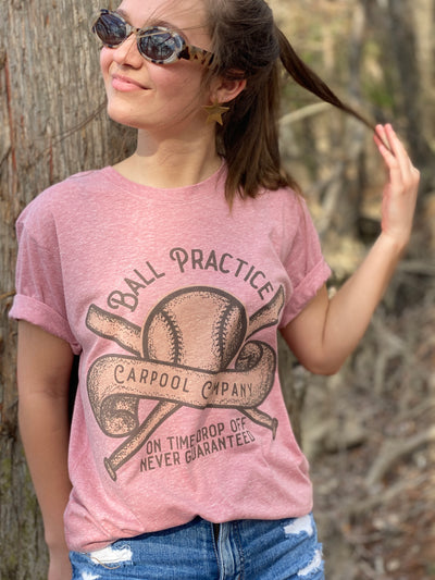Heather Pink tee. Graphic has a baseball with two bats crossed behind it and a banner across the baseball that says carpool company. Text above the graphic says Ball practice and underneath it says on time drop off never guaranteed. Graphic is rust and dark brown with dark brown text.