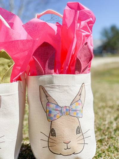 Canvas easter basket with cloth bunny ears with a graphic of a bunny wearing a bow with multicolored squares on it. 