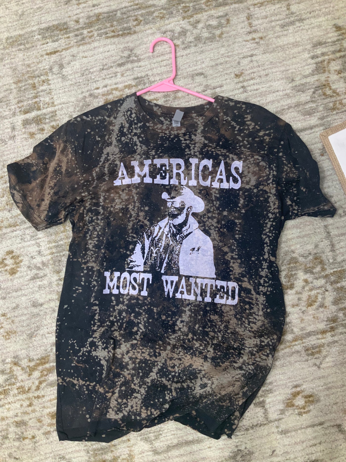 Black Bleach Dyed shirt. Graphic says Americas most wanted with a photo of Rip from Yellowstone in brown.