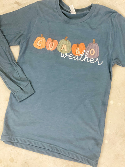 A long sleeve stonewash blue tee with a fall graphic. There are five different colored pumpkins each with a different letter that spells out the word gumbo and underneath the word weather in a white cursive font