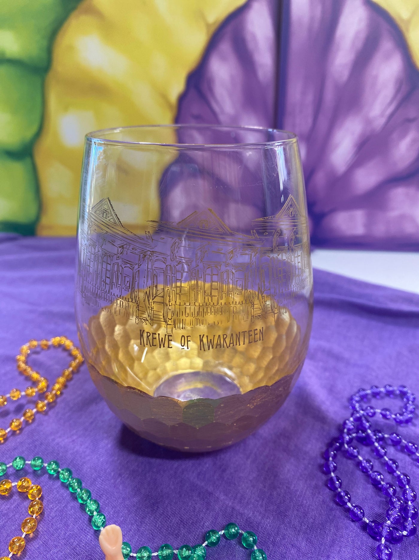 A stemless wine glass with gold on the bottom and a graphic of historic New Orleans houses and the words Krewe of Kwaranteen underneath in gold