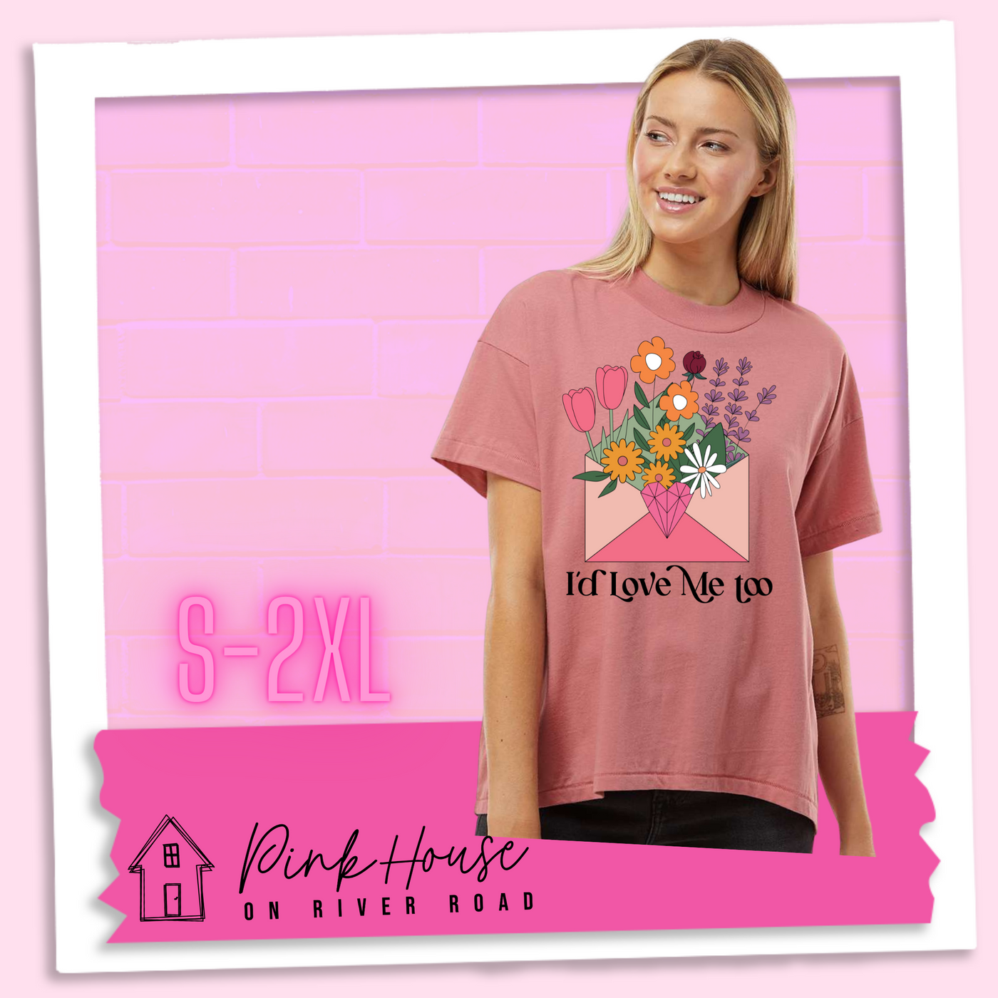 A blonde woman in an oversized mauve HiLo tee with a graphic of a pink envelope filled with different types of flowers and a geometric heart seal. Text underneath reads "I'd Love Me Too"