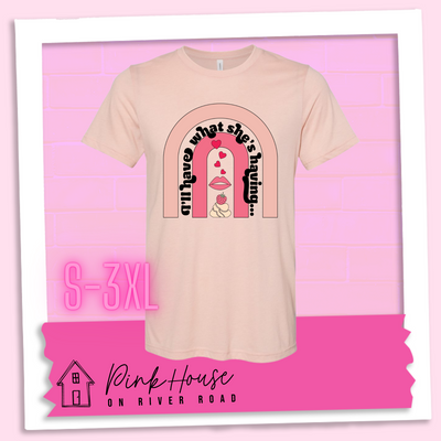 Heather peach tee with a graphic of a strawberry dessert and a set of lips with hearts, there is a pink arch going over the art. There is a retro font arched over the pink art that says "I'll have what she's having..." in black with another arch above that in light pink.