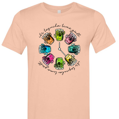Peach tee with a graphic. Graphic has a clock in the center with multicolored margaritas instead of numbers and around the outside of the clock are the words "It's tequila time y'all" in black cursive font.