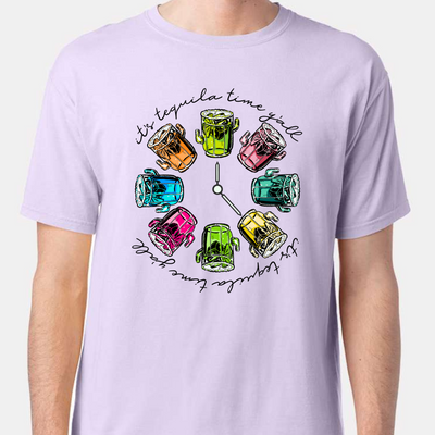 Lavender tee with a graphic. Graphic has a clock in the center with multicolored margaritas instead of numbers and around the outside of the clock are the words "It's tequila time y'all" in black cursive font.