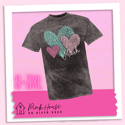 Black Mineral wash tee with 3 different colored leopard print hearts in various sizes in the lower right hand corner of the graphic is the word Muah in light punk script