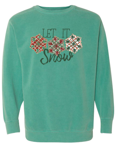 Green Sweatshirt with the words Let It in think block letters at the top with three snowflakes underneath. Far left snowflake is red with beige stripes and a green snowflake design on the top, Middle snowflake is green with white stripes and a dark red snowflake design on the top, and the right snowflake is white with red stripes and a dark green snow flake design on top and the word snow in a brush script underneath.