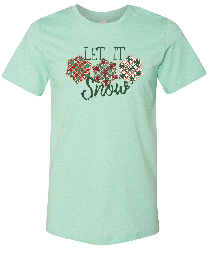 Mint tee with the words Let It in think block letters at the top with three snowflakes underneath. Far left snowflake is red with beige stripes and a green snowflake design on the top, Middle snowflake is green with white stripes and a dark red snowflake design on the top, and the right snowflake is white with red stripes and a dark green snow flake design on top and the word snow in a brush script underneath.
