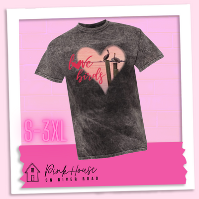 Black Mineral Wash tee with graphic. Graphic is a pink heart with a photo of some pelicans standing on post in the water. To the left of the heart are the words love birds in a pink cursive font and the O in love has been replaced with a heart.