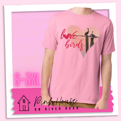 Cotton Candy Pink tee with graphic. Graphic is a pink heart with a photo of some pelicans standing on post in the water. To the left of the heart are the words love birds in a pink cursive font and the O in love has been replaced with a heart.