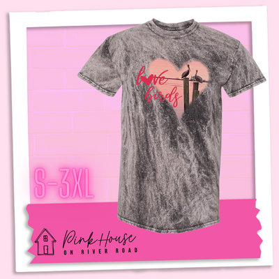 Charcoal Mineral Wash tee with graphic. Graphic is a pink heart with a photo of some pelicans standing on post in the water. To the left of the heart are the words love birds in a pink cursive font and the O in love has been replaced with a heart.