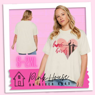 An oversized cream HiLo tee with graphic. Graphic is a pink heart with a photo of some pelicans standing on post in the water. To the left of the heart are the words love birds in a pink cursive font and the O in love has been replaced with a heart.