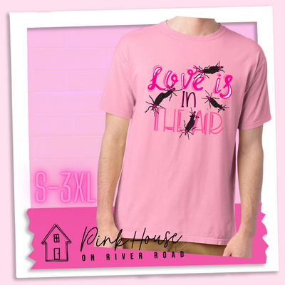 Cotton Candy Pink Tee with Graphic. Graphic says " Love Is in the Air". "Love Is" is a hot pink cursive font with white highlights and hot pink accent lines underneath is the word "In" Is it in a black font with a hot pink highlight. on the bottom is "The Air" in Light pink with light pink accent lines. There are also black flying bugs with hot pink spots behind their heads