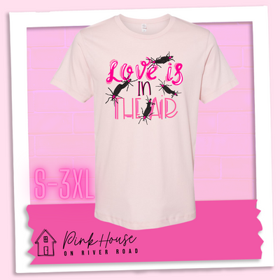 Faded Pink Tee with Graphic. Graphic says " Love Is in the Air". "Love Is" is a hot pink cursive font with white highlights and hot pink accent lines underneath is the word "In" Is it in a black font with a hot pink highlight. on the bottom is "The Air" in Light pink with light pink accent lines. There are also black flying bugs with hot pink spots behind their heads