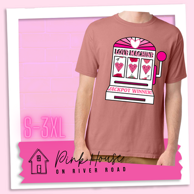 Mauve Tee with a graphic. Graphic is of a white slot machine with pink accents at the top of the slot machine is an arch with different shades of pink and a heart cut out of the middle. Underneath the are are the words Love machine in hot pink with white dots to look like lights. the reels of the slot machines show three geometric hearts. The slot pull has a pink base with a white handle and pink knob on it. Under the reels are the words Jackpot Winner in pink.