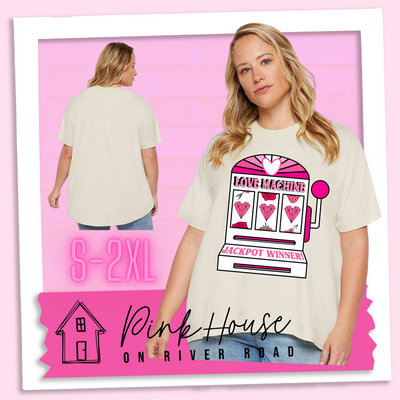 A cream oversized HiLo Tee with a graphic. Graphic is of a white slot machine with pink accents at the top of the slot machine is an arch with different shades of pink and a heart cut out of the middle. Underneath the are are the words Love machine in hot pink with white dots to look like lights. the reels of the slot machines show three geometric hearts. The slot pull has a pink base with a white handle and pink knob on it. Under the reels are the words Jackpot Winner in pink.