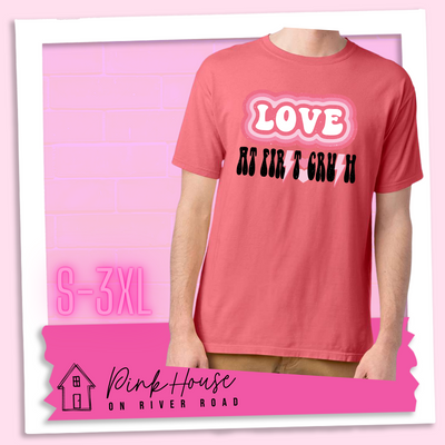 Coral Tee. The graphic has the word Love in retro bubble letters with differetn colored pink outlines radiating from the word, underneath are the worxs at first in black with the s in first replaced with a pink lightning bolt, then there are three different colored hearts followed by the word crush in the same black font with the S replaced with the same pink lightening bolt.