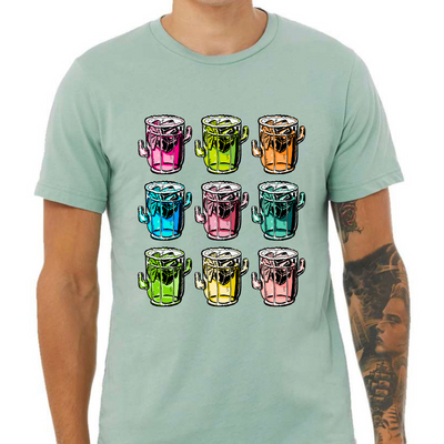 A dusty blue tee with a graphic. Graphic is of 9 margarita glasses, 3 rows of 3, all shaped like cactus with ice cubes, limes and salt on the rim, all 9 glasses are a different color.