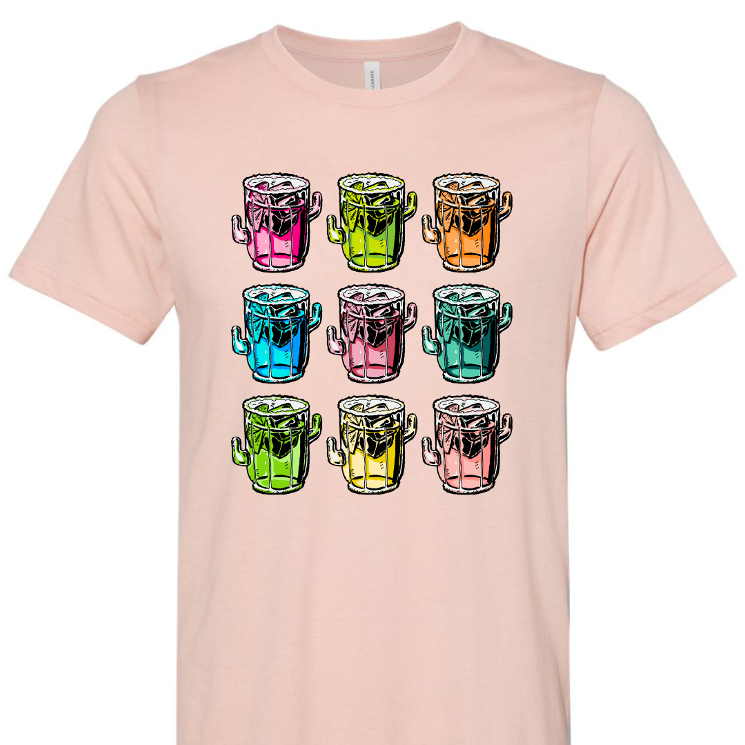 A peach tee with a graphic. Graphic is of 9 margarita glasses, 3 rows of 3, all shaped like cactus with ice cubes, limes and salt on the rim, all 9 glasses are a different color.