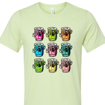 A spring green tee with a graphic. Graphic is of 9 margarita glasses, 3 rows of 3, all shaped like cactus with ice cubes, limes and salt on the rim, all 9 glasses are a different color.