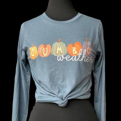A long sleeve stonewash blue tee with a fall graphic. There are five different colored pumpkins each with a different letter that spells out the word gumbo and underneath the word  weather in a white cursive font