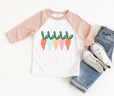 A white raglan with peach sleeves and a graphic of five different colored balloon carrots